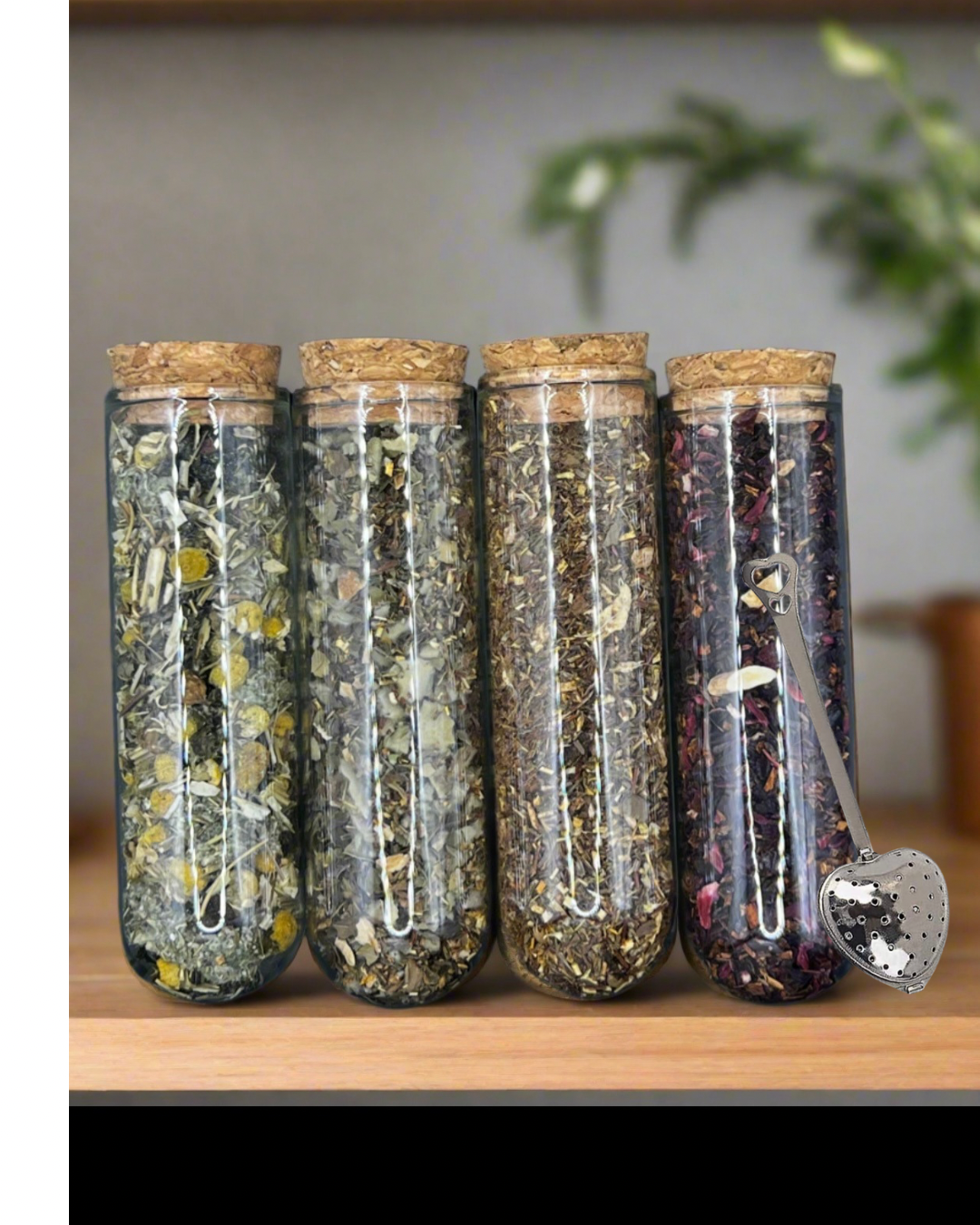 Four glass jars with cork lids containing various loose leaf herbs on a wooden surface and heart shaped tea steeper